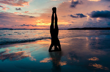 A person doing a headstand on a beach at sunset